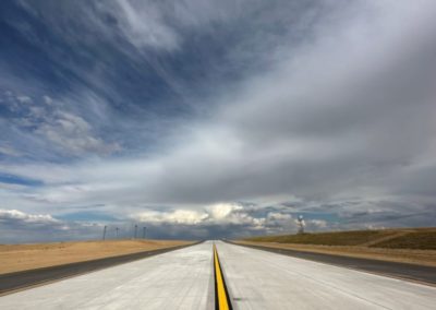 An empty road in Denver, CO, with a prominent yellow line dividing the lanes under a clear blue sky.