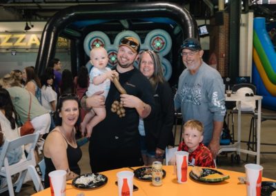 A family is posing happily with food at the Brannan Companies picnic in Denver, CO